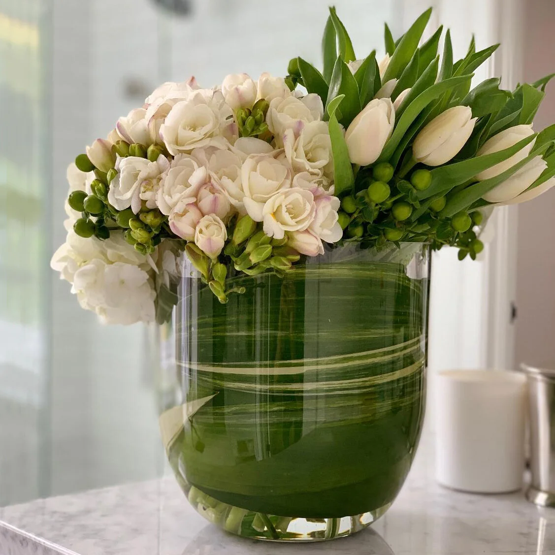 White roses and parrot tulips in leaf-lined glass